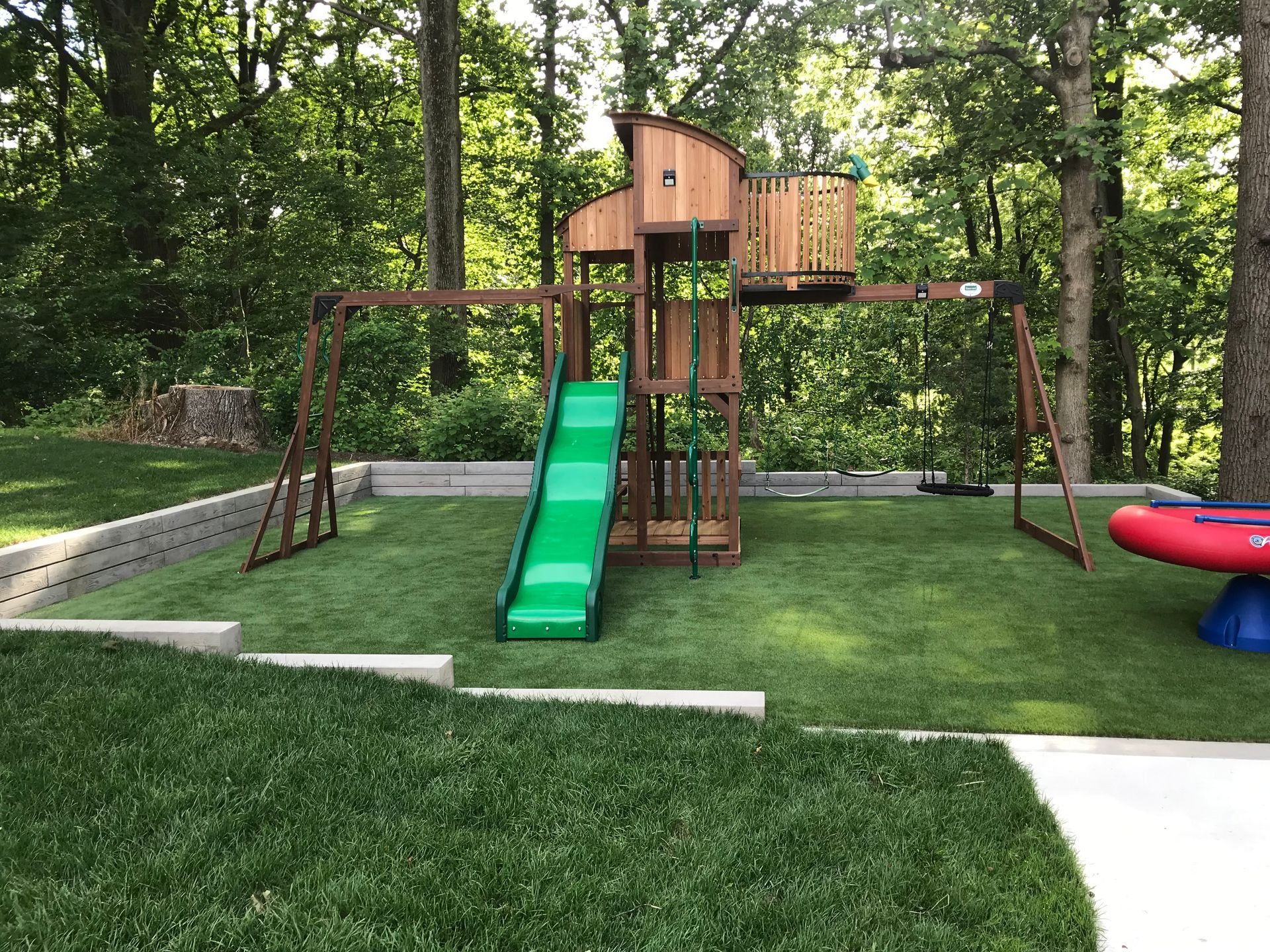 Backyard playground with wooden playset, green slide, and red spinning seat on a grassy lawn.