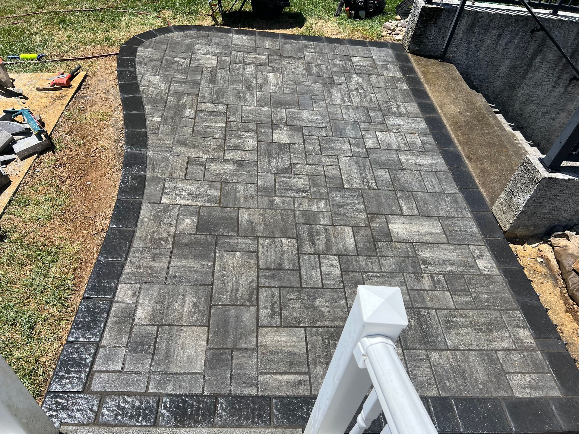 Freshly paved gray interlocking stone driveway with dark border and a white railing in the foreground