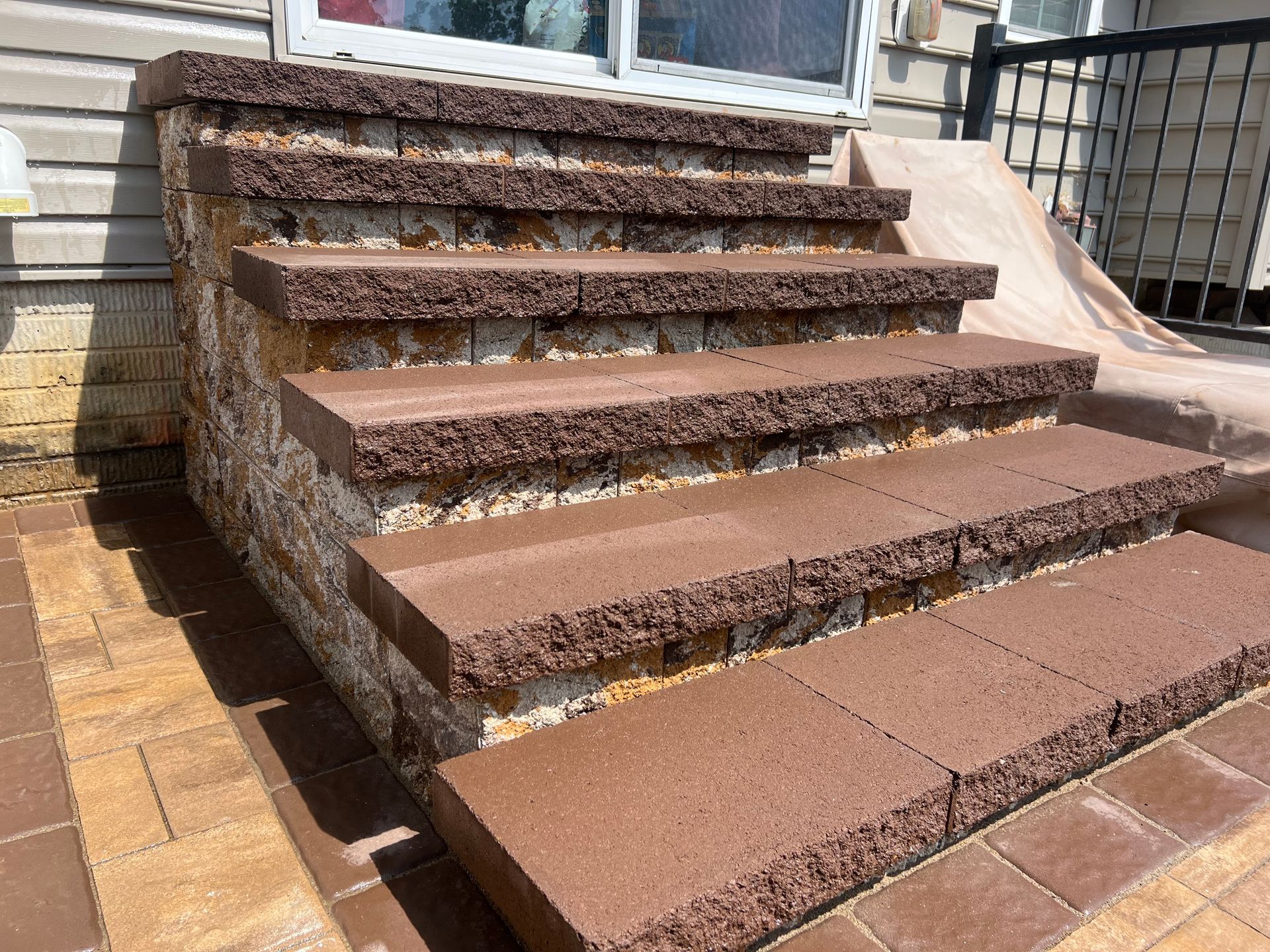 Outdoor front steps with brown textured treads and brick pavers, showing rough stone sides and a house entrance