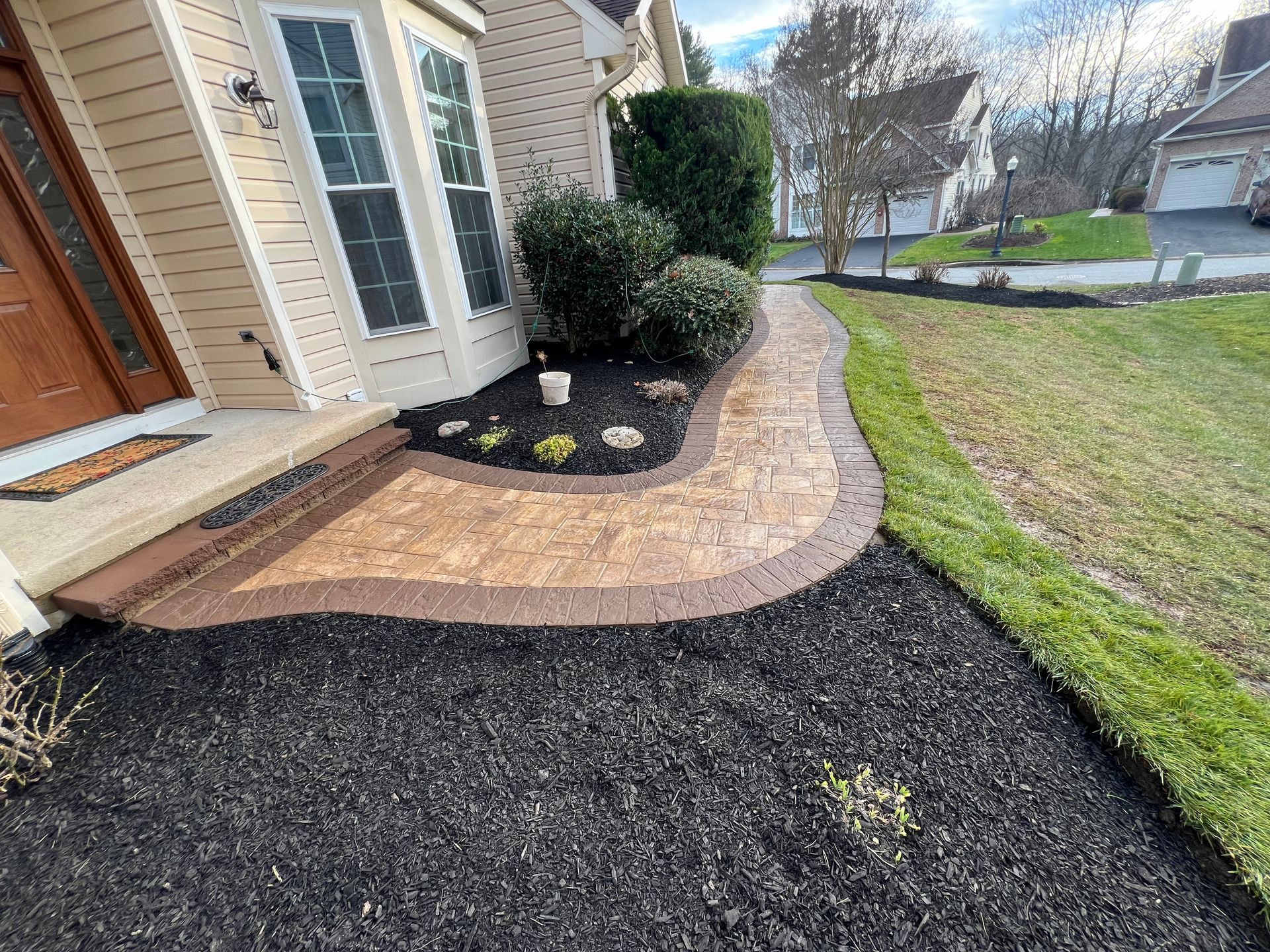 Curved stone garden path beside a house, bordered by dark mulch and green lawn.