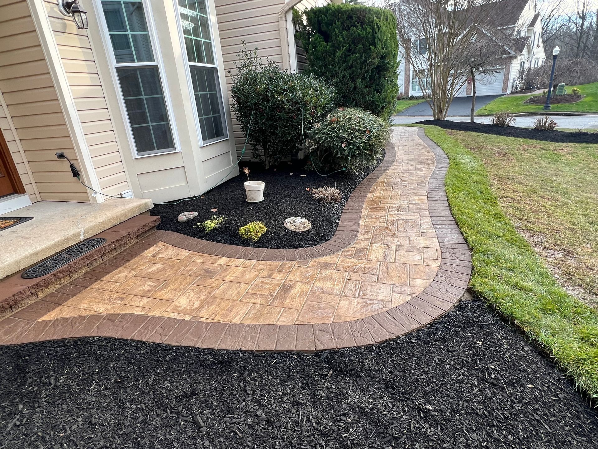 Brick walkway curving along a house with black mulch beds and trimmed shrubs