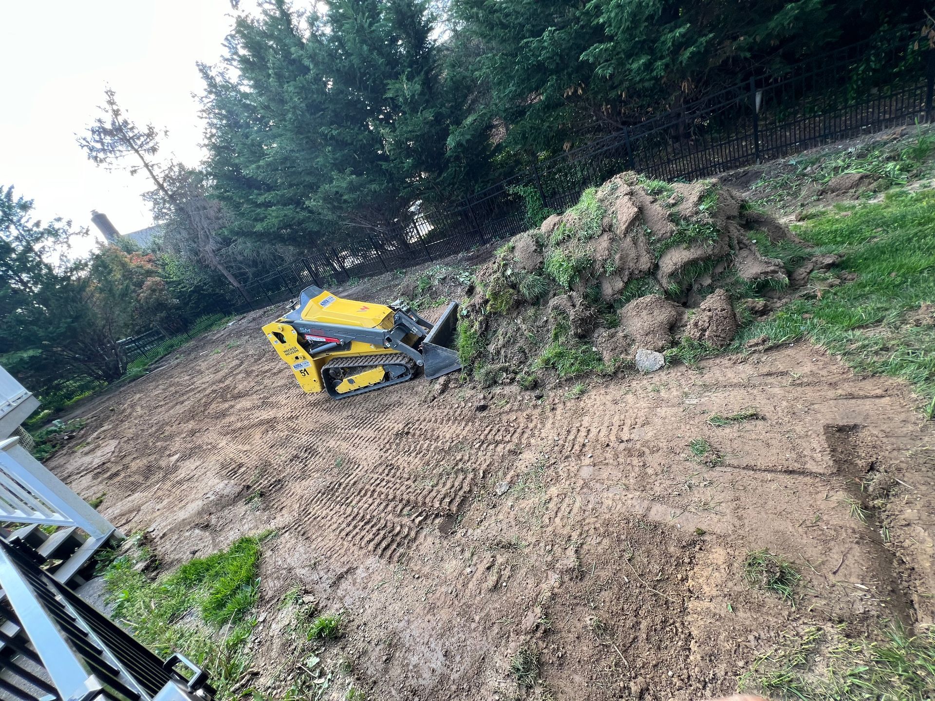 Yellow mini excavator beside a dirt pile on a grassy, wooded slope