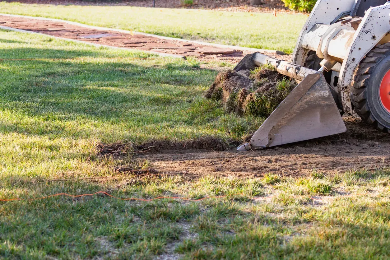 Small loader scooping dirt on a grassy field, leaving a patchy disturbed area