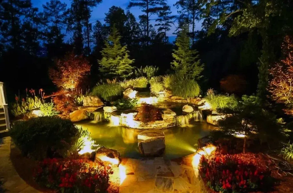 Illuminated garden at night with glowing pathway, trees, shrubs, and colorful flower beds