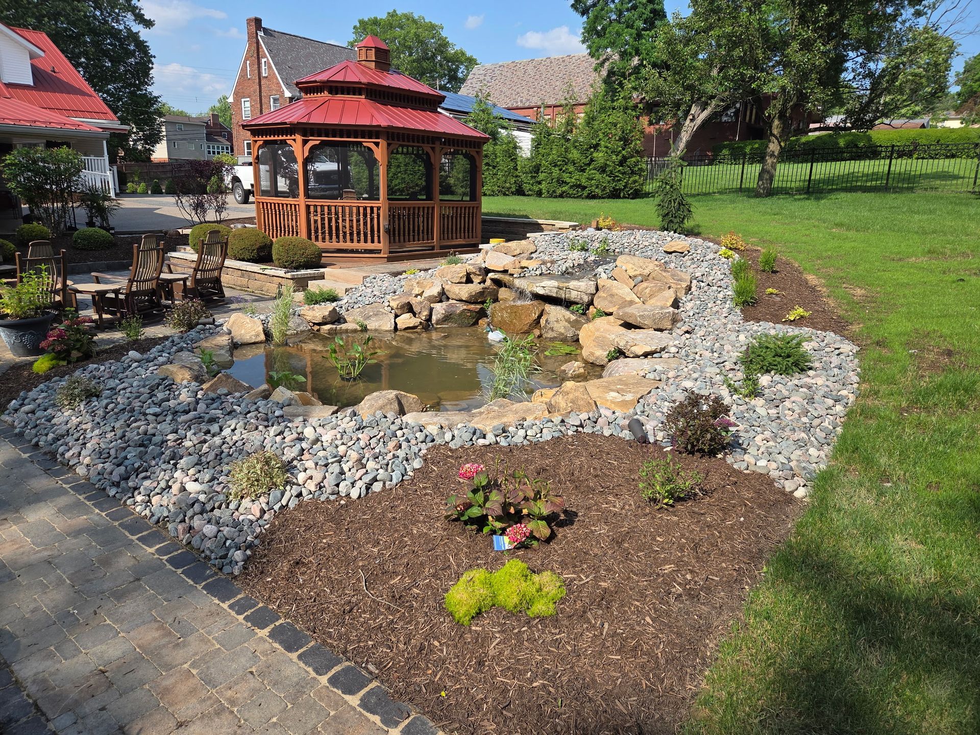 A gazebo is sitting in the middle of a garden next to a pond.