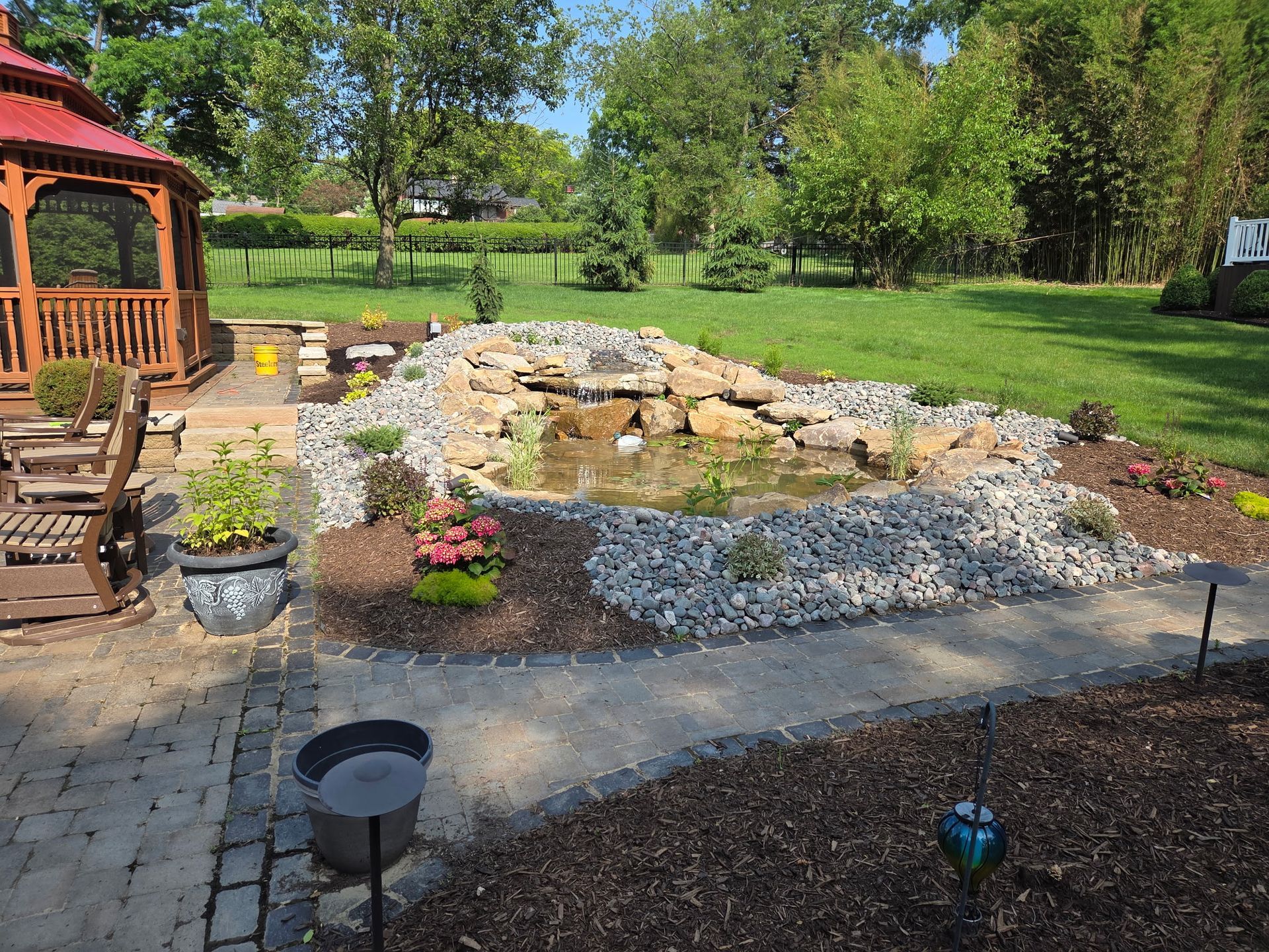 There is a gazebo in the backyard with a pond in the middle of it.