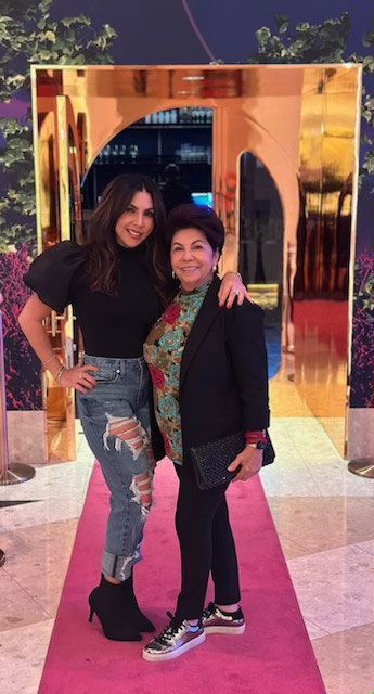 Two women are standing next to each other on a pink carpet.