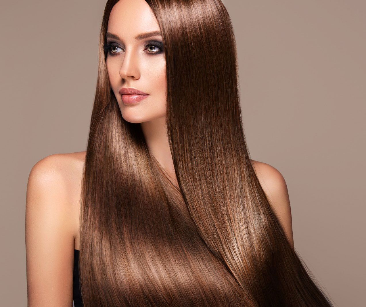 A woman with very long brown hair is standing in front of a brown background.