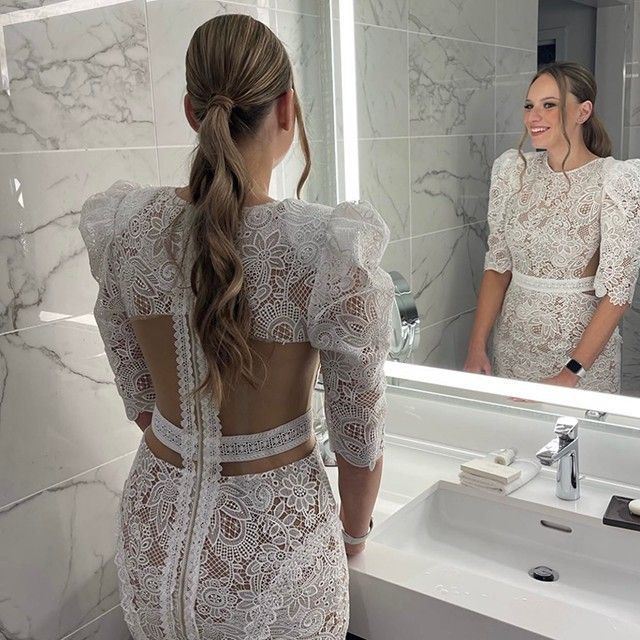 A woman in a white lace dress is standing in front of a mirror