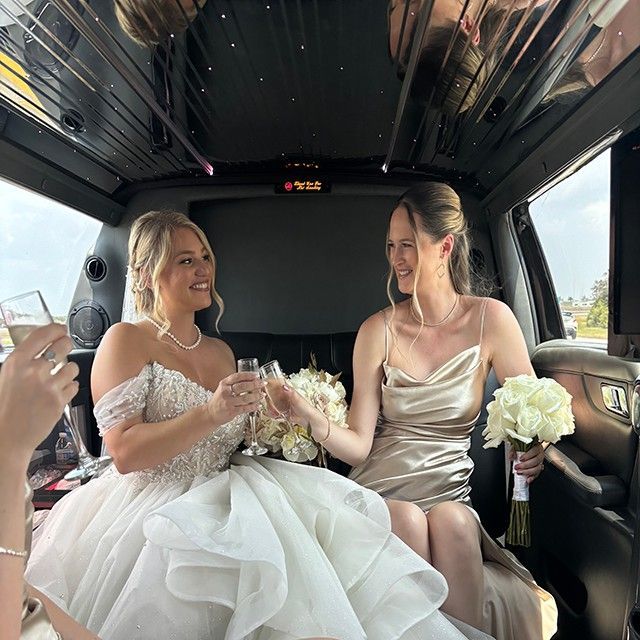 A bride and her bridesmaid are toasting in a limousine