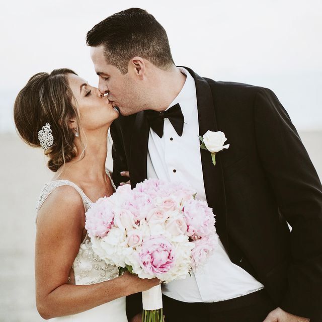 A bride and groom kissing while holding a bouquet of pink and white flowers