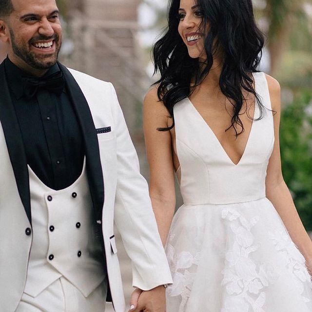 A man in a tuxedo and a woman in a white dress are holding hands