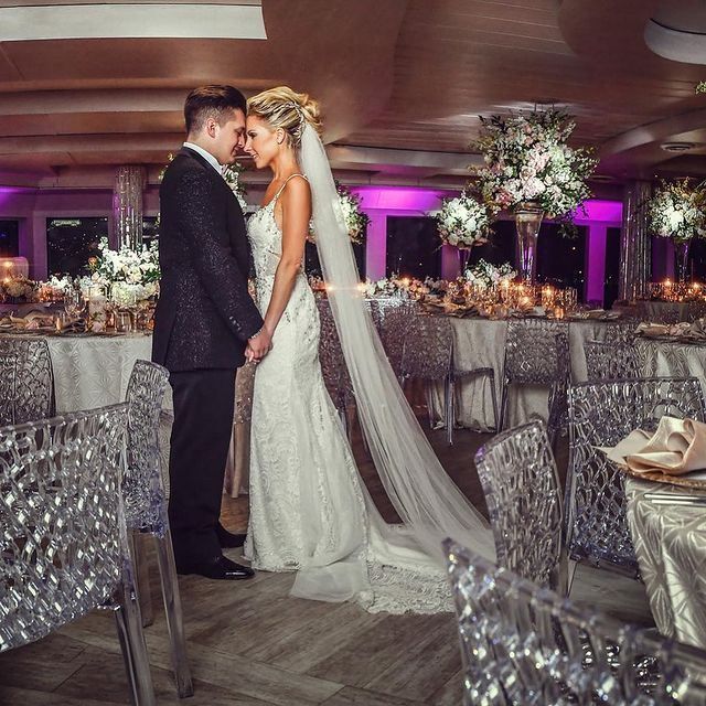 A bride and groom are standing in a room with tables and chairs