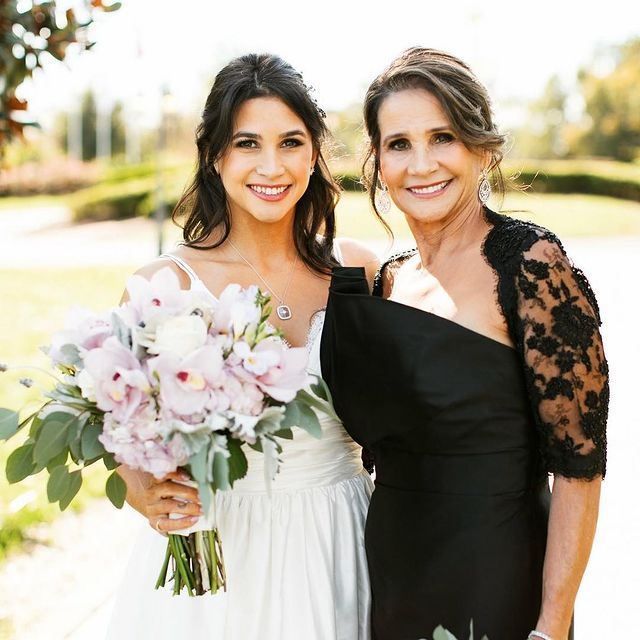 A bride and her mother are posing for a picture