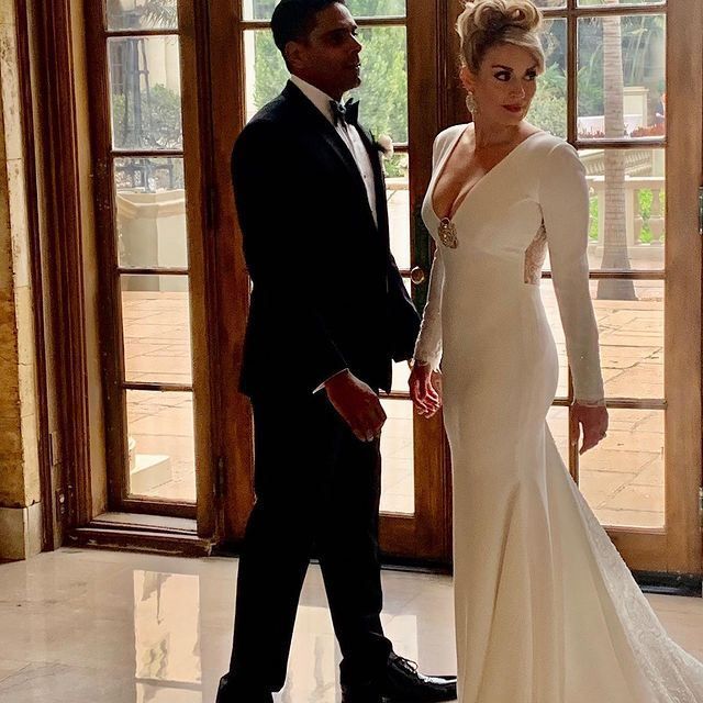 A bride and groom standing next to each other in front of a window
