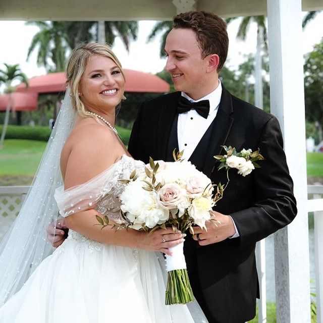 A bride and groom pose for a picture under a gazebo