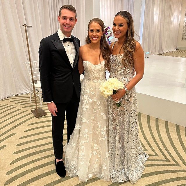 A bride and groom pose for a picture with a man in a tuxedo