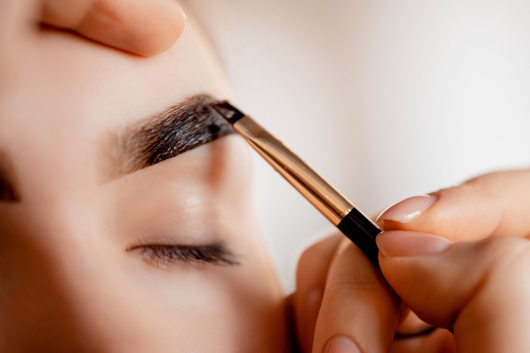 A woman is applying eye shadow to her eyebrows with a brush.