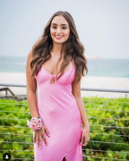 A woman in a pink dress is standing in front of a beach.