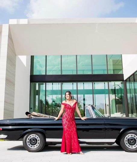 A woman in a red dress is standing next to a black car