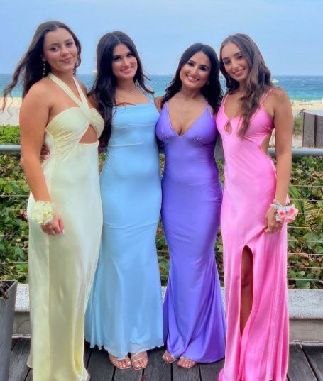 Four women are posing for a picture while wearing different colored dresses.