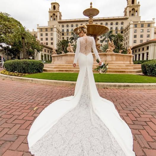 A woman in a wedding dress is standing in front of a fountain