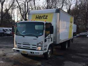 A white and yellow Hertz truck is parked in a parking lot