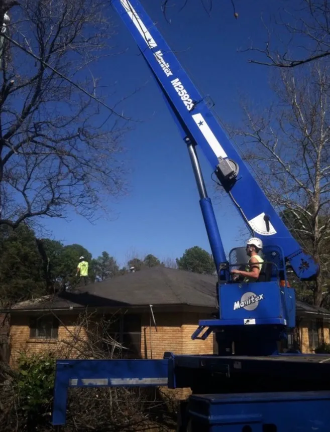 Man in a lift operating near a roof, with another person on the roof. Blue lift against a sunny sky.