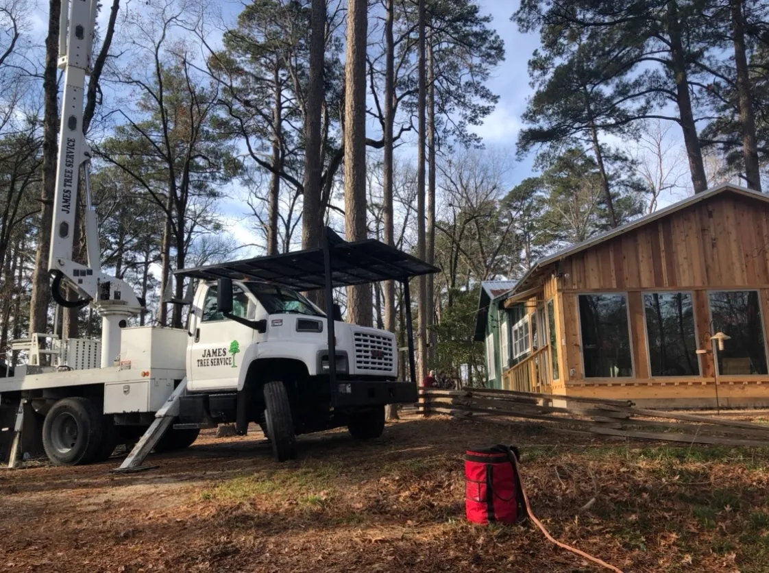 A white truck with a crane near a cabin in a wooded area on a sunny day.