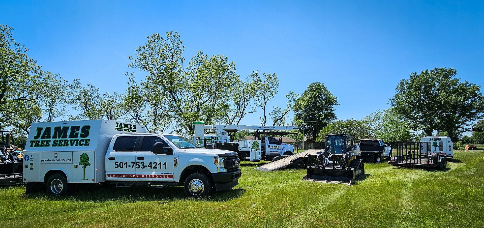 White work trucks and equipment on green grass, clear blue sky; James Tree Service.