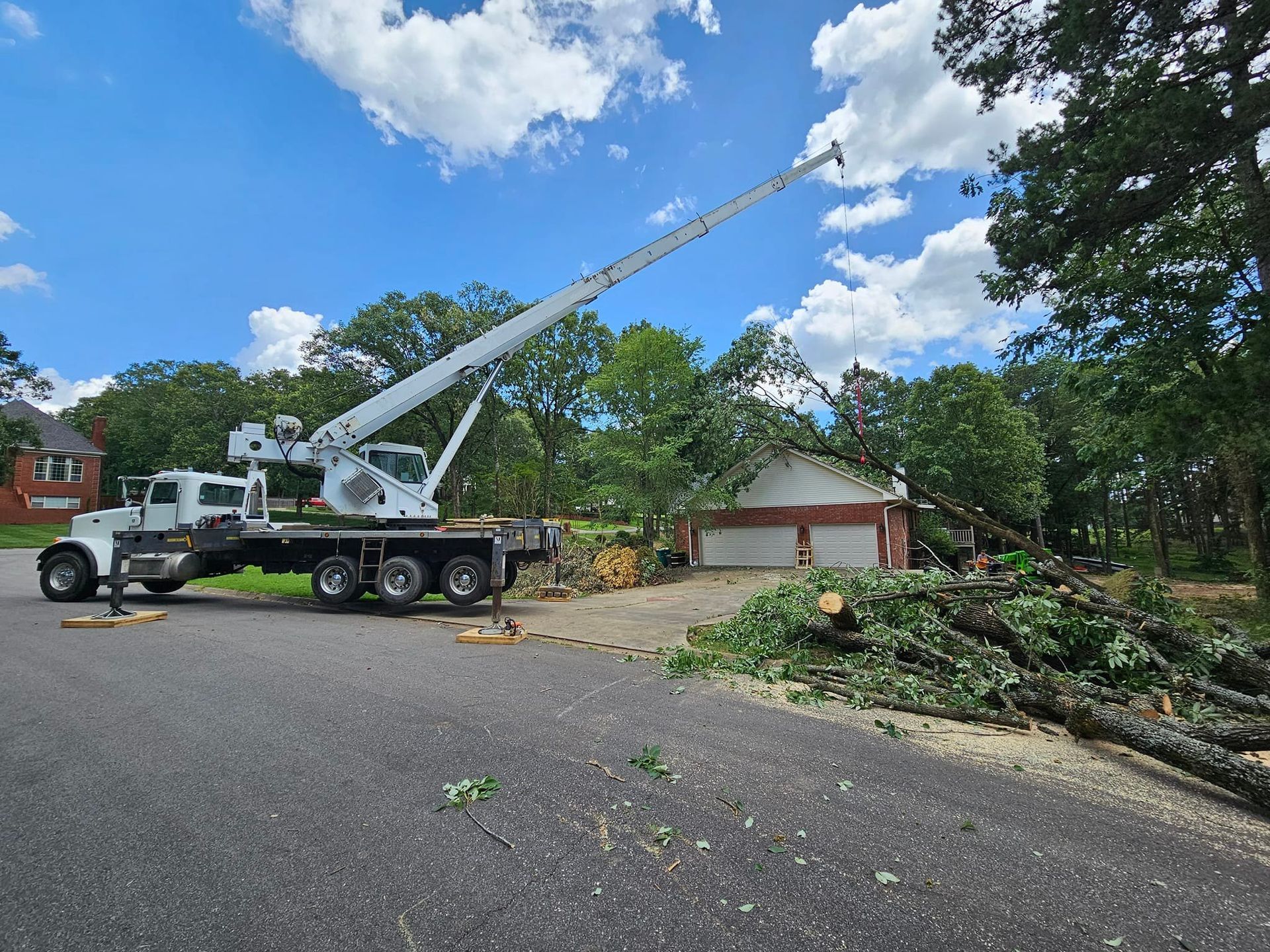 A crane truck removing a fallen tree from a garage on a sunny day.