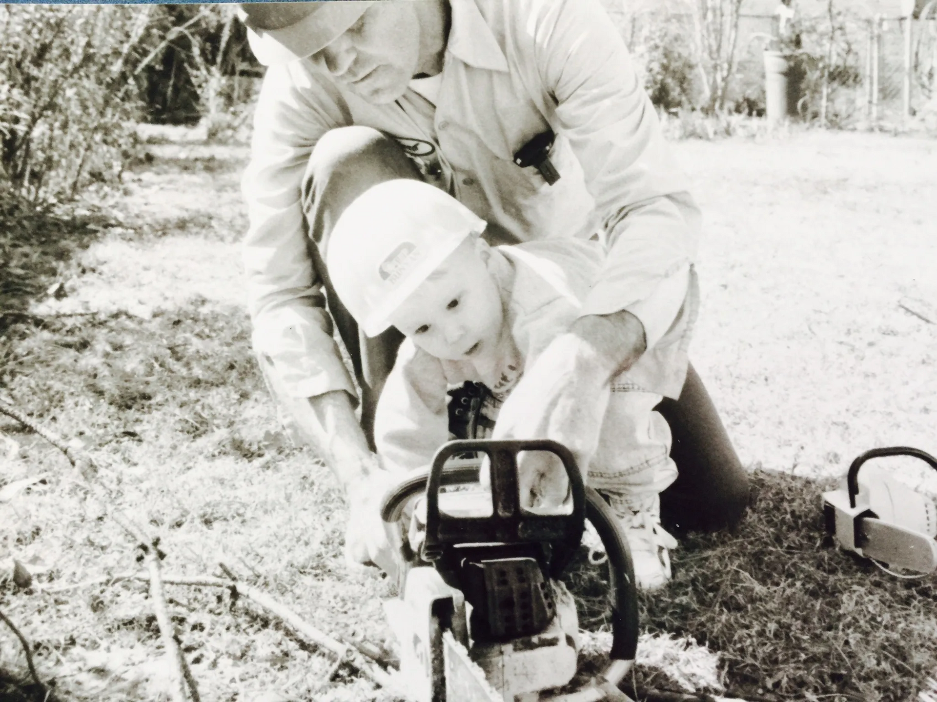 Man teaching a young child how to use a chainsaw outdoors.