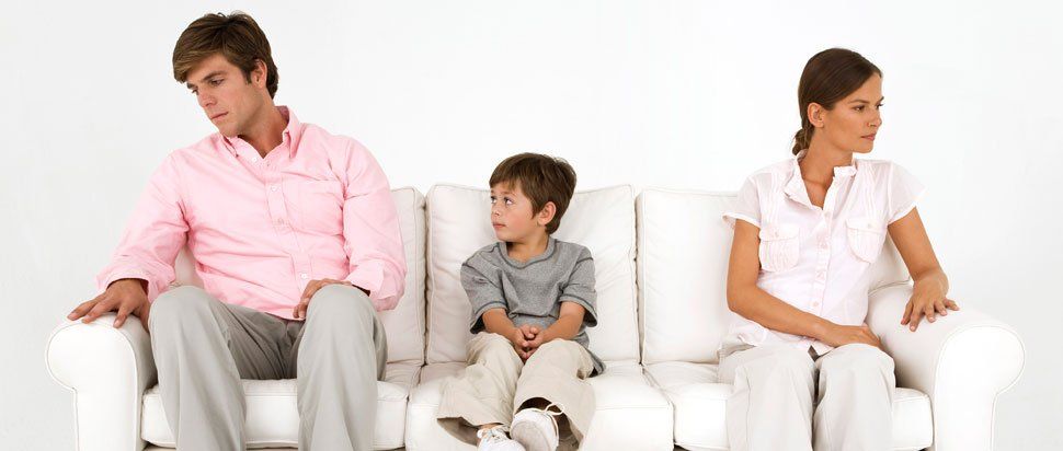 Man and woman sitting on opposite ends of a couch with a young boy sitting in between them