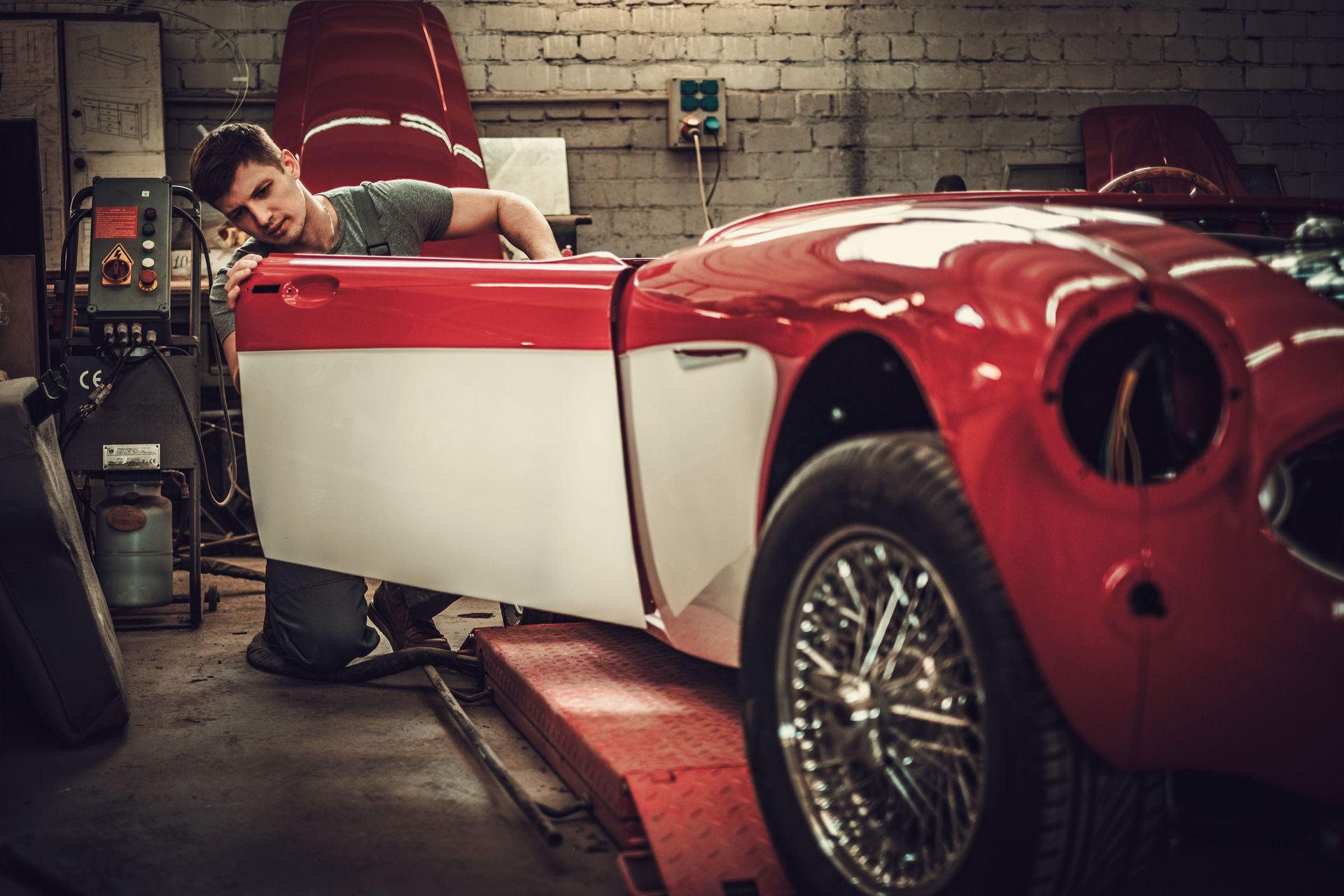 Man inspecting red and white vintage car door in a garage.