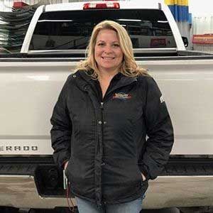 Woman in black jacket standing in front of a white truck, smiling.