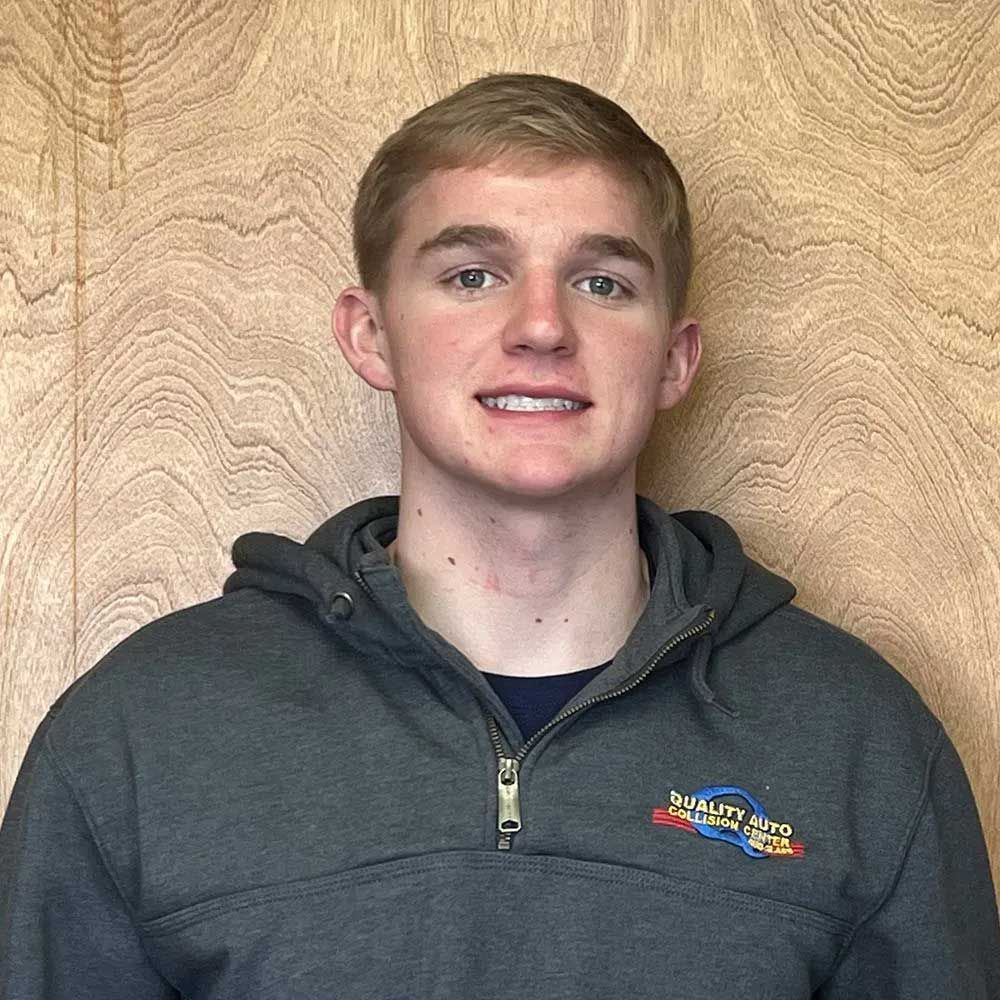 Blond person in gray hooded sweatshirt smiling, against wood background.