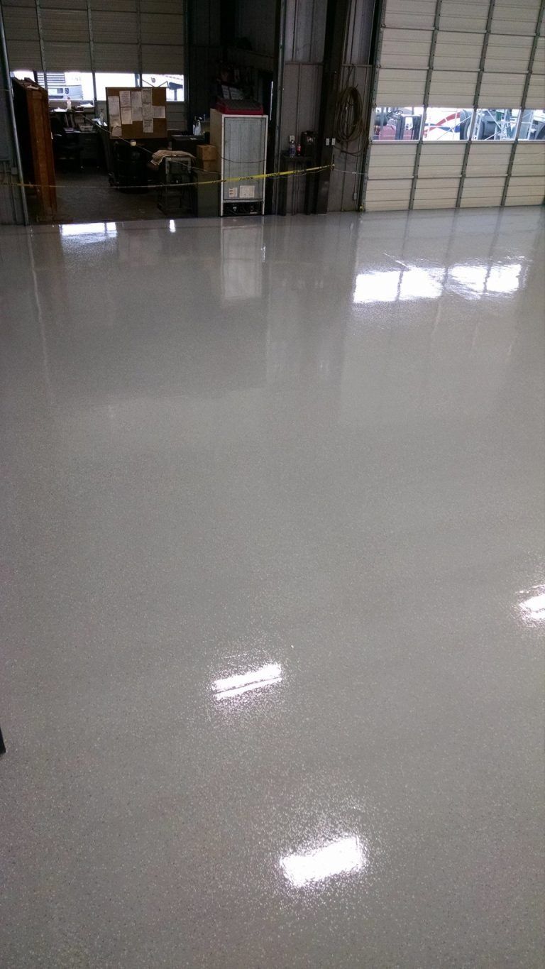 A shiny white floor in a garage with a garage door in the background.