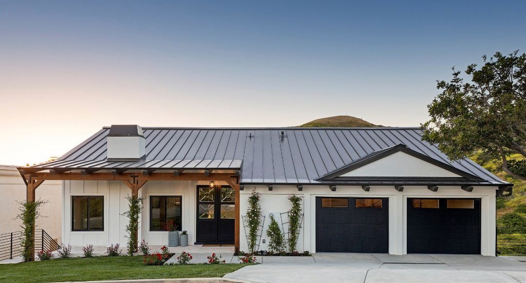 A white house with a black garage door and a metal roof.