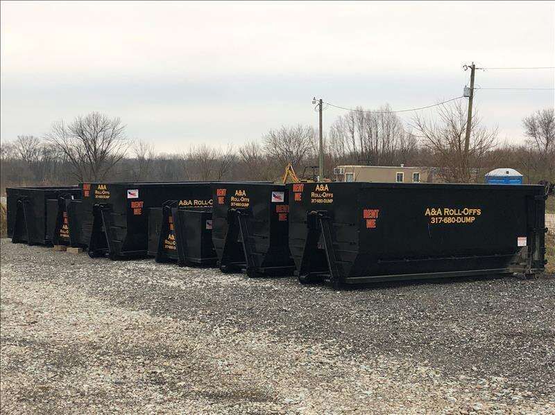 A row of dumpsters are lined up in a gravel lot.