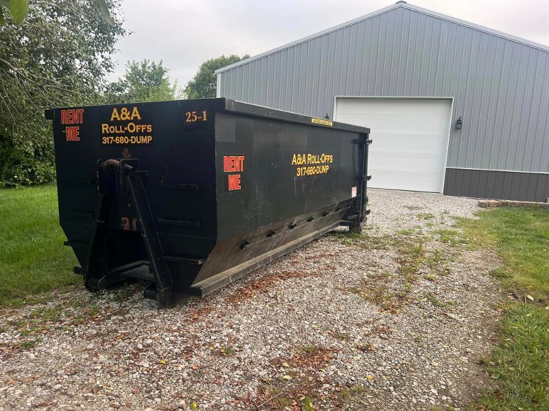 A large black dumpster is sitting in front of a garage.