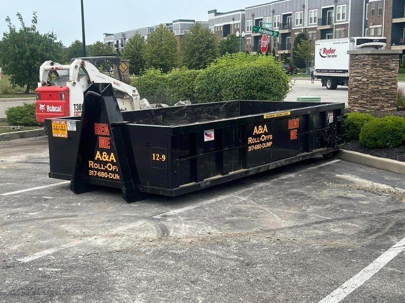 A dumpster is parked in a parking lot next to a bulldozer.