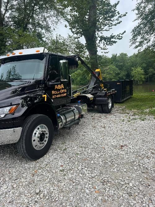 A black tow truck is parked on gravel next to a dumpster.