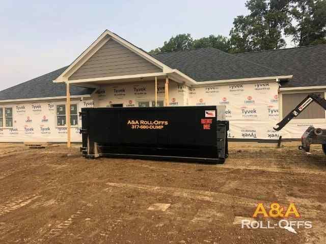 A dumpster is parked in front of a house under construction.
