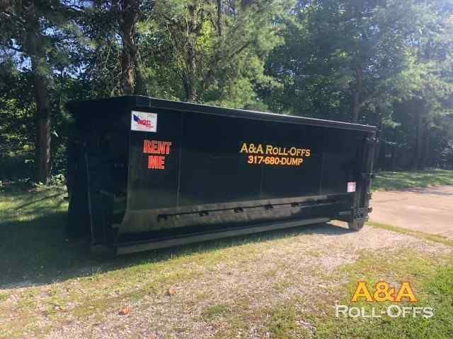 A black dumpster is parked in a grassy area next to trees.