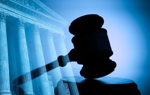 Silhouette of a judge’s gavel before courthouse columns in blue light