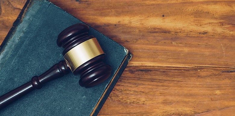 Judge’s gavel resting on a green book atop a wooden surface