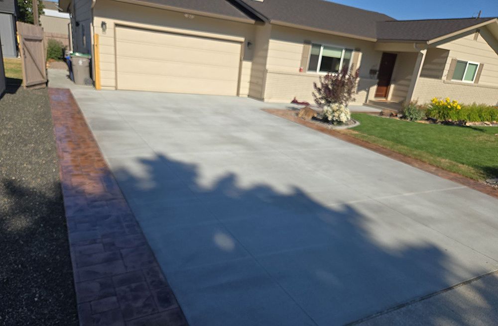Concrete driveway with a decorative border next to a house on a sunny day.