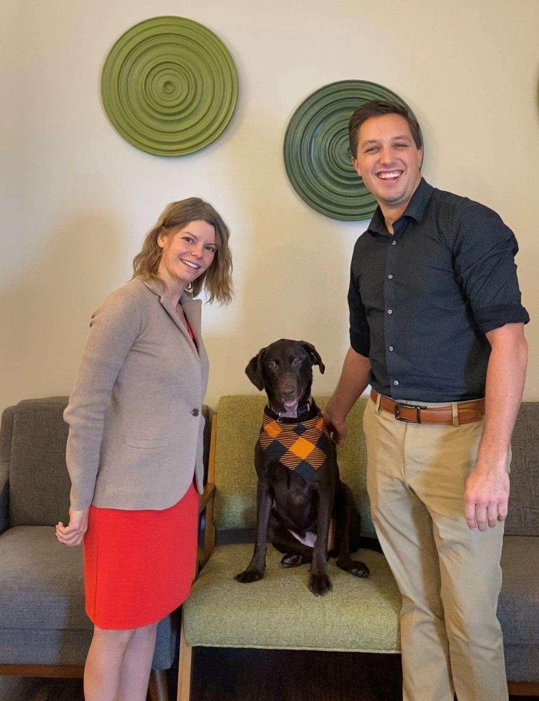 A man and woman standing next to a dog in a chair