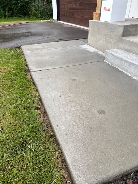 Concrete walkway leading to steps and a building with a dark wood door, next to green grass.