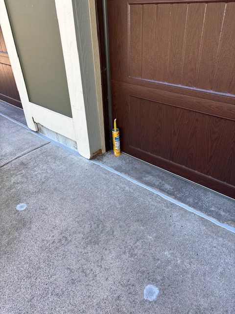 A tube of yellow caulk next to a brown garage door on a concrete driveway.